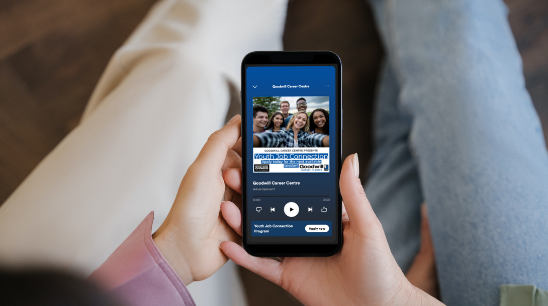 Someone's arm holding an iPhone with the screen showing a Goodwill Spotify ad.
