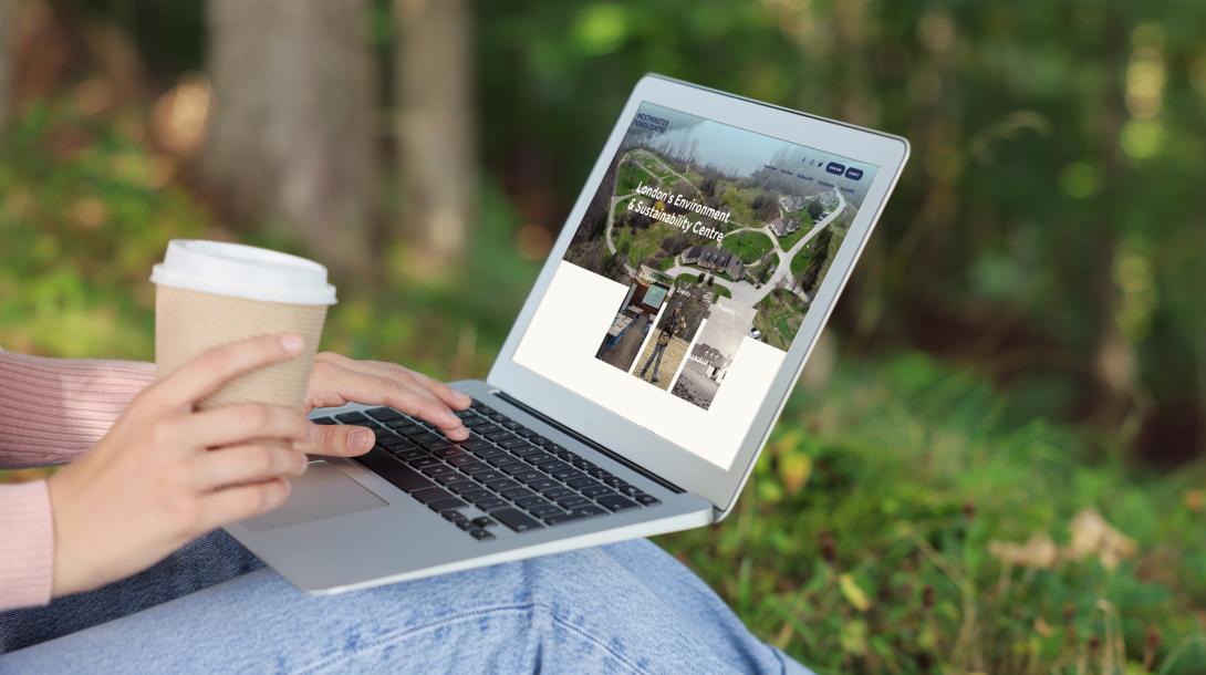 Person sitting in forest with Westminster Ponds Website on laptop